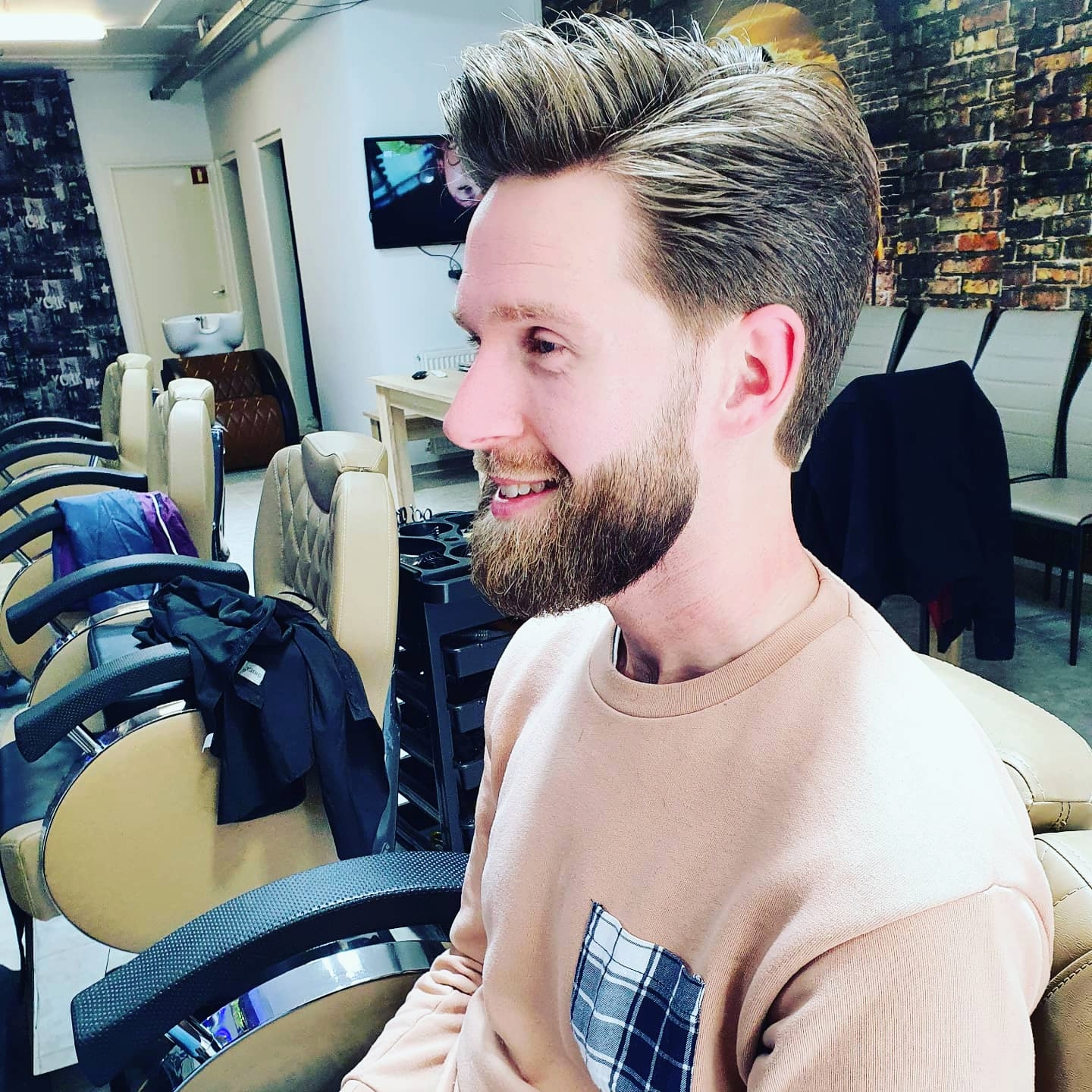 Lachende klant met een gestylede kuif en volle baard in de kappersstoel