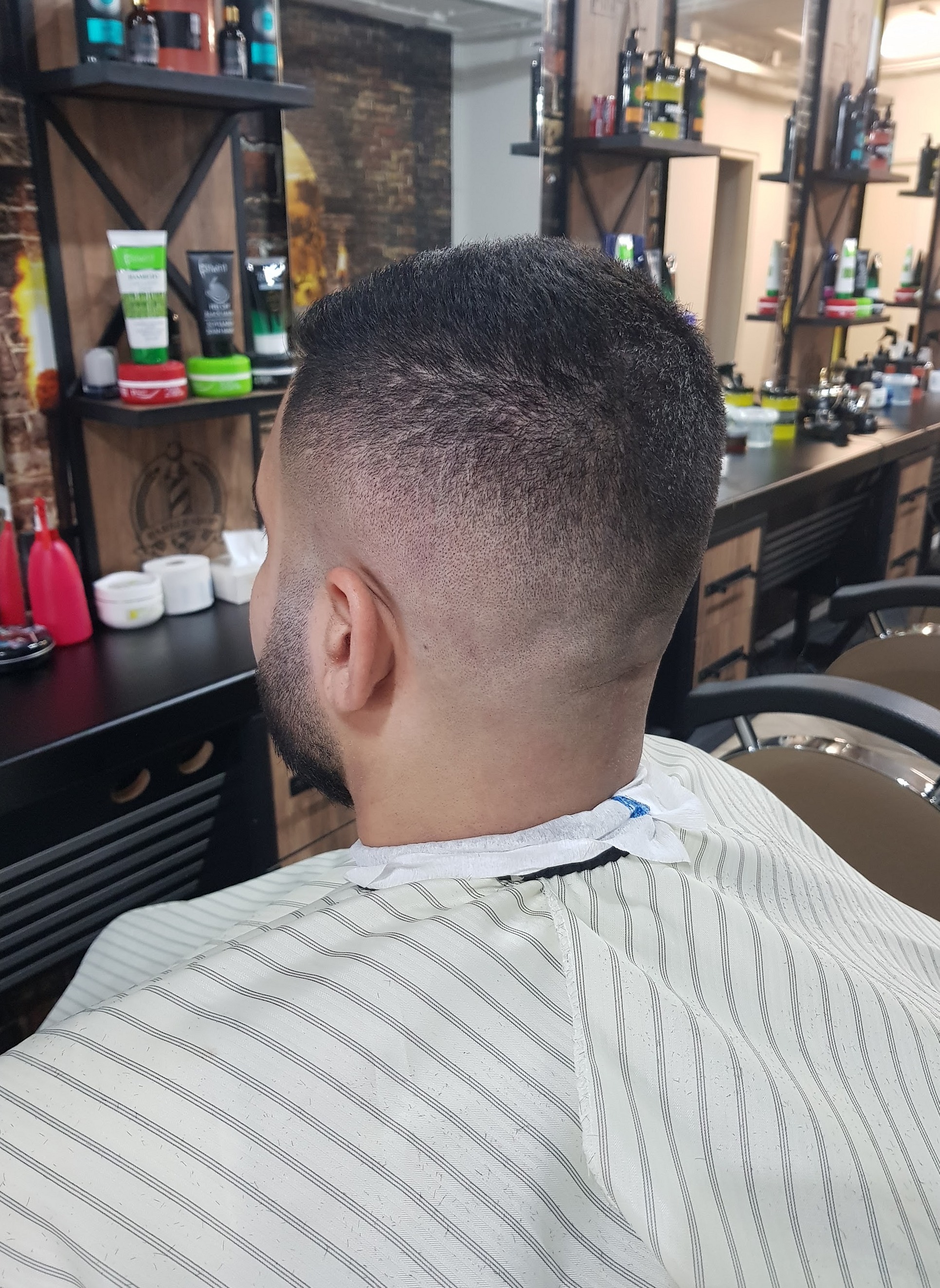 Een korte fade van achteren, klant met een gestreepte kapmantel